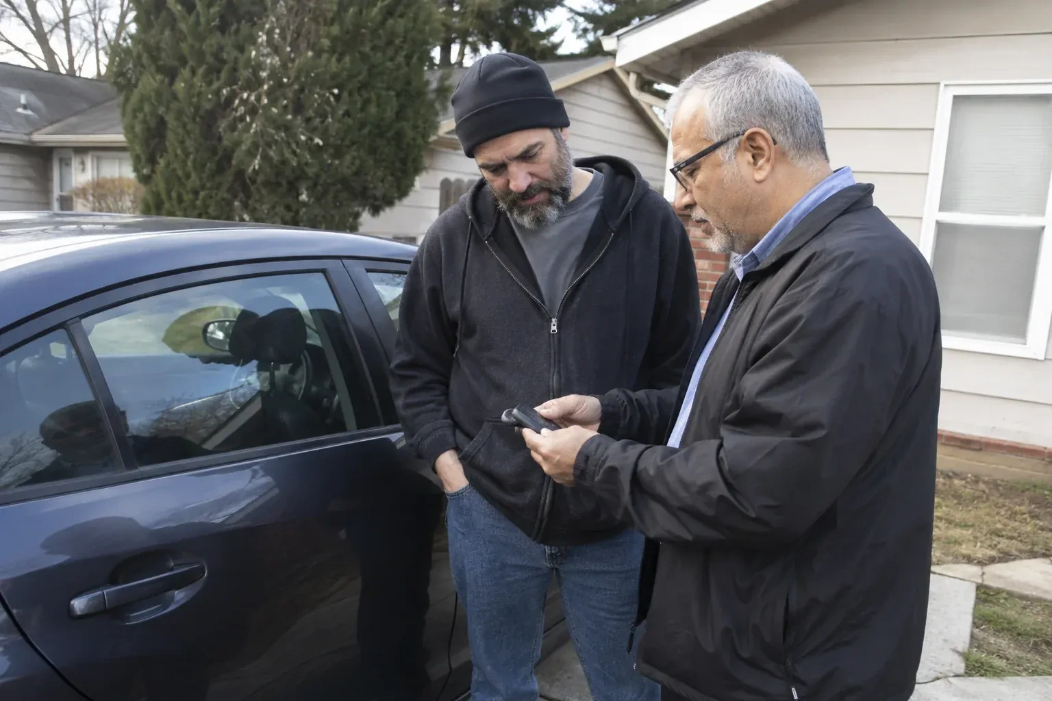 Two adults discussing a key fob beside a parked car. — Car Lockout Service, Halton Hills