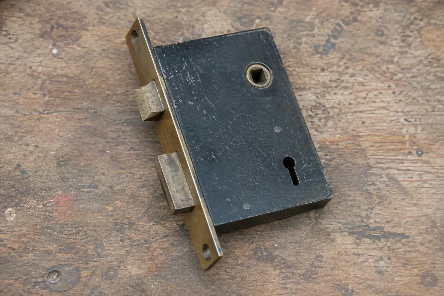 Closed mortise lock case with spindle opening, keyhole, latch and deadbolt on a wooden workbench. — Vintage Mortise Lock Service, Halton Hills